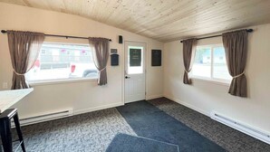 Een kamer met houten plafond, twee ramen met gordijnen, een deur en een kleine tafel.