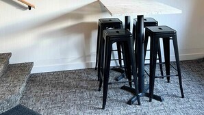 Een eetgedeelte met een witte tafel, zwarte stoelen, een raam met gordijn en een houten plafond.