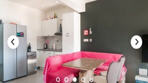 Una cocina moderna con armarios blancos, un refrigerador de acero inoxidable y un comedor con una mesa cubierta con un mantel rosa.