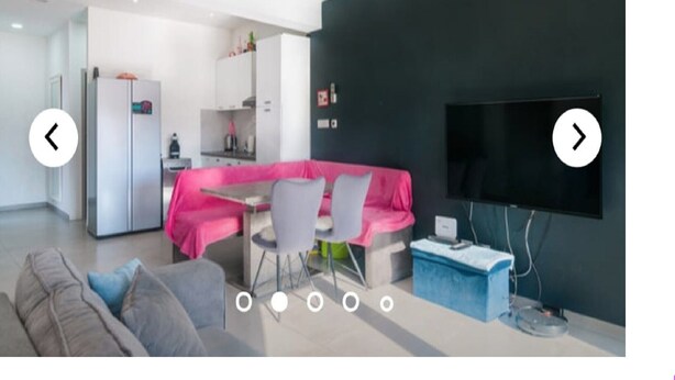 Una sala moderna con un sofá gris, un sofá modular rosa y una zona de comedor con mesa y sillas.