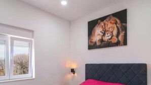 Un dormitorio con cama, ventana, un cuadro e iluminación en la pared.