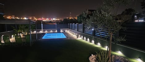 Vista nocturna de un área de piscina en la azotea, con una despejada vista del horizonte de la ciudad al fondo.