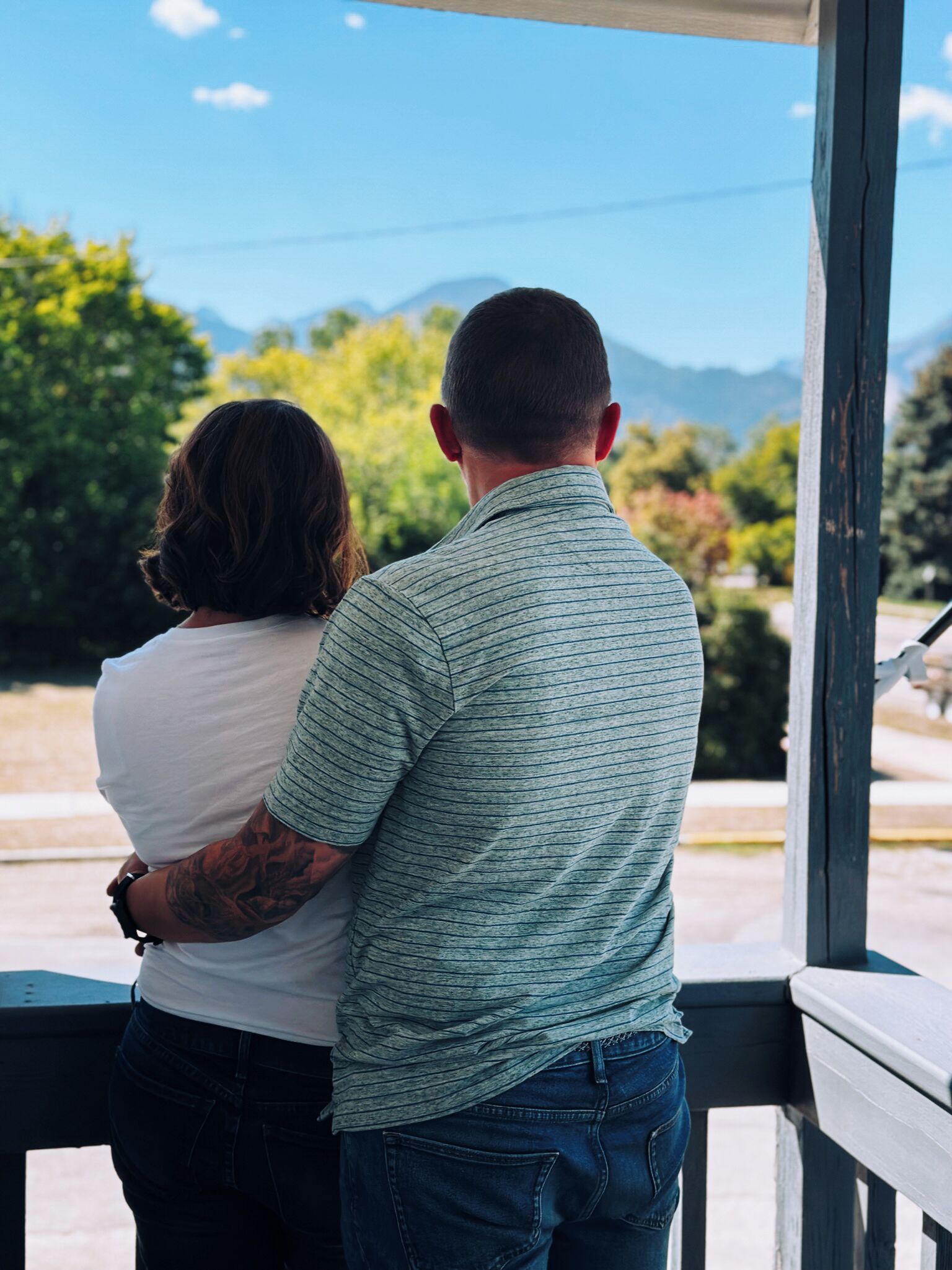 Una pareja de pie en un balcón con vistas a árboles y montañas.