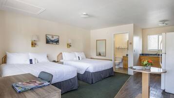 A hotel room with two beds, a small table, a chair, a desk, a mirror, a sink, and a window.
