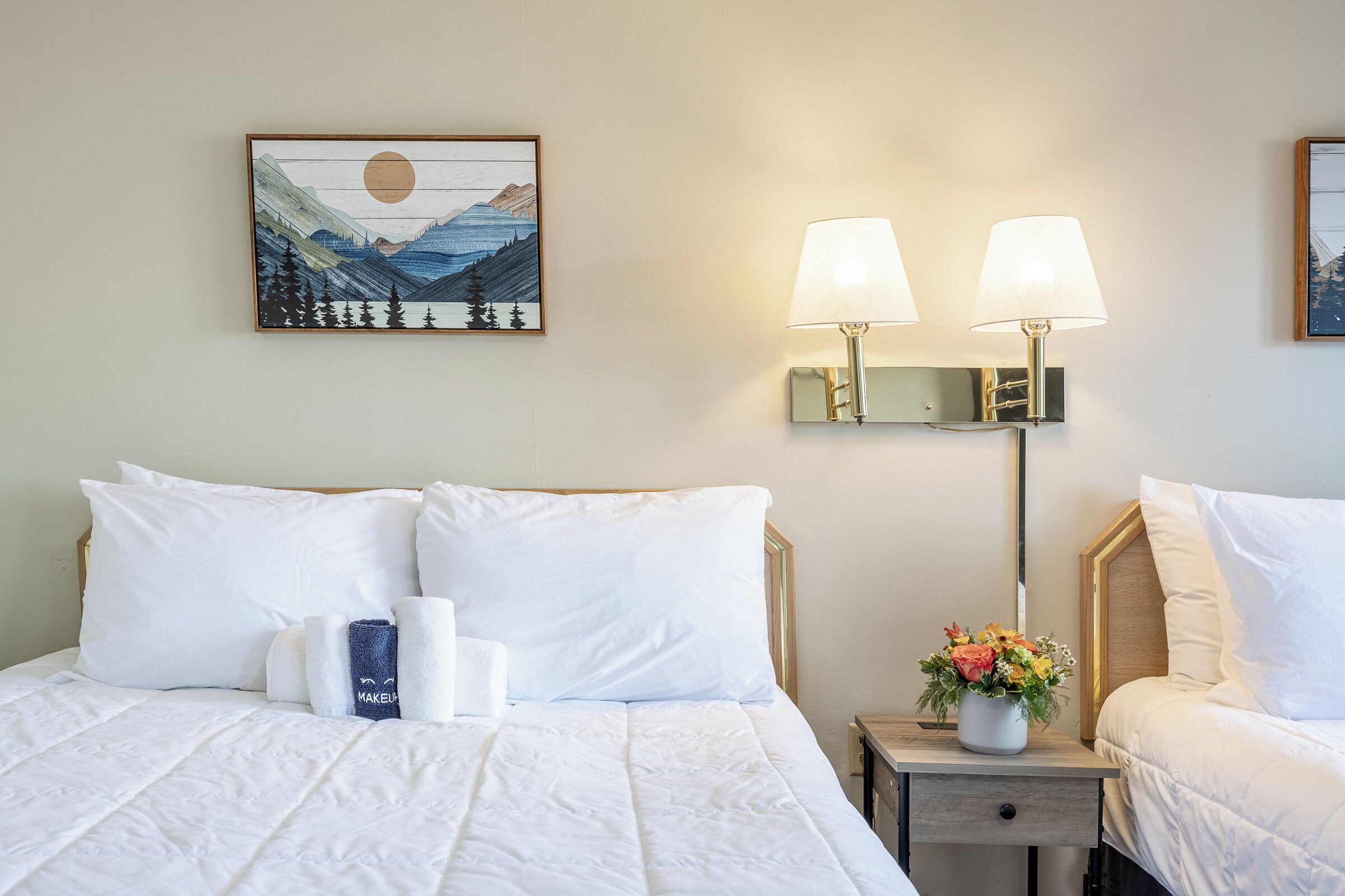 A neatly made bed with white bedding, a nightstand with a lamp, and a framed picture on the wall.
