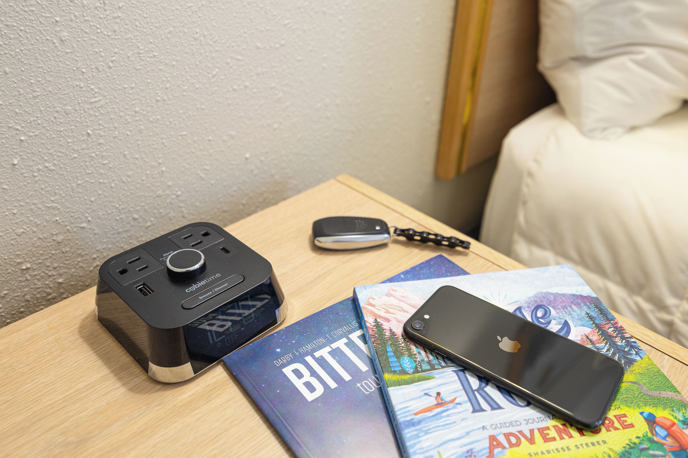 A wooden nightstand with a portable charger, a smartphone, and two books.