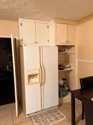 Kitchen area with a refrigerator, upper cabinets, and dining table.