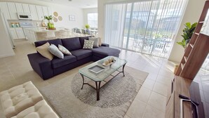 A modern living room with a dark sofa, a glass coffee table, and a white armchair. - Lovely Villa at Kissimmee (Kissimmee)