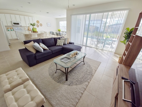 A modern living room with a dark sofa, a glass coffee table, and a white armchair.