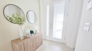 A hallway with a wooden console table, two round mirrors, a potted plant, and a door with blinds. - Lovely Villa at Kissimmee (Kissimmee)