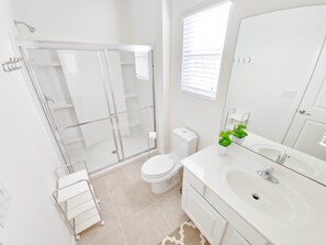 A modern bathroom with a glass shower enclosure, a toilet, a sink with a mirror, and a small potted plant. - Lovely Villa at Kissimmee (Kissimmee)
