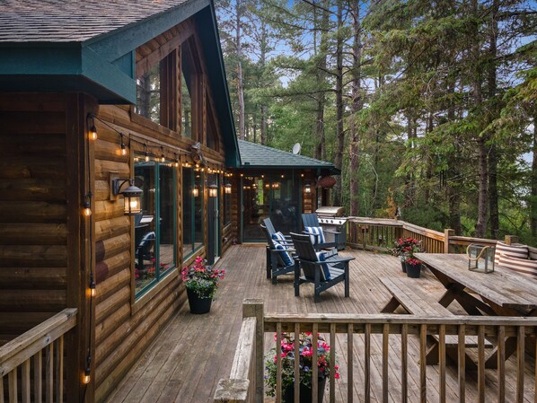 Een houten blokhut met terras, zitplaatsen buiten en een barbecuehoek.