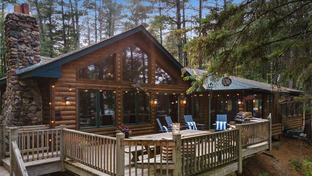 A log cabin with a deck, outdoor seating, and a stone chimney.