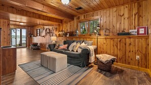 A cozy cabin interior with a wooden interior, a sofa, ottoman, and a dining area with a table and chairs.