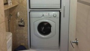 Uma lavanderia compacta com duas máquinas de lavar empilhadas e um vaso sanitário.