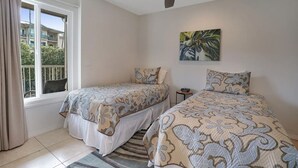 Une chambre avec deux lits, un ventilateur de plafond, une fenêtre avec des rideaux et un tableau au mur.