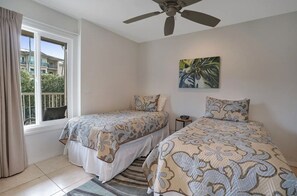 Quarto com duas camas, um ventilador de teto, uma janela com cortinas e um quadro na parede.