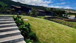 A modern house with a stone staircase, a well-maintained lawn, and a view of the surrounding hills. - Casas da Prainha   A (Prainha de Baixo)