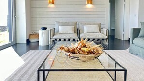 A modern living room with a glass coffee table, two sofas, a basket of dried corn and flowers, and two wall-mounted lamps. - Casas da Prainha   A (Prainha de Baixo)