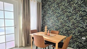 A dining area with a table and chairs, a window with curtains, and a wall with a leafy pattern.