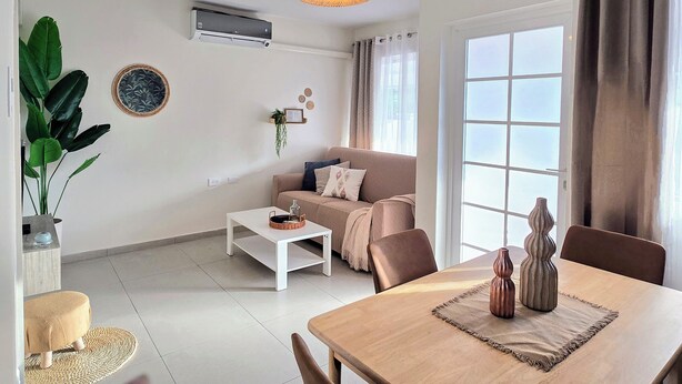 A modern living room with a sofa, coffee table, dining table, and a hanging light fixture.