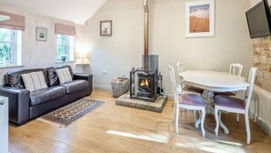 Una sala de estar acogedora con chimenea, una mesa de comedor con sillas, un sofá con cojines y un televisor montado en la pared.