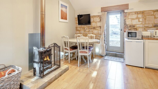 Una cocina acogedora con pared de piedra, chimenea, mesa de comedor con sillas, televisor montado en la pared y microondas en la encimera.