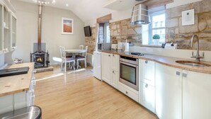 Una cocina moderna con pared de piedra, suelo de madera y una zona de comedor con sillas blancas.
