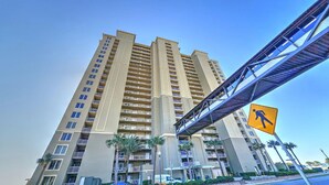 Un edificio residencial alto con varios balcones, una señal de paso para peatones y un cielo azul despejado.