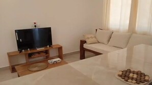 A living room with a flat-screen TV on a wooden stand, a sofa with cushions, and a tray of chocolates on the floor. - Dacha Diani Paradise 2 (Diani)