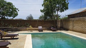 A rectangular swimming pool with a stone border, surrounded by lounge chairs and a brick wall. - Dacha Diani Paradise 2 (Diani)