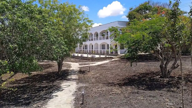 A building with a white facade and arched windows, surrounded by trees and a dirt path. - Dacha Diani Paradise 2 (Diani)
