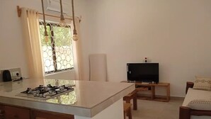 A compact kitchen with a gas stove, a small TV, and a dining area with wooden chairs. - Dacha Diani Paradise 2 (Diani)