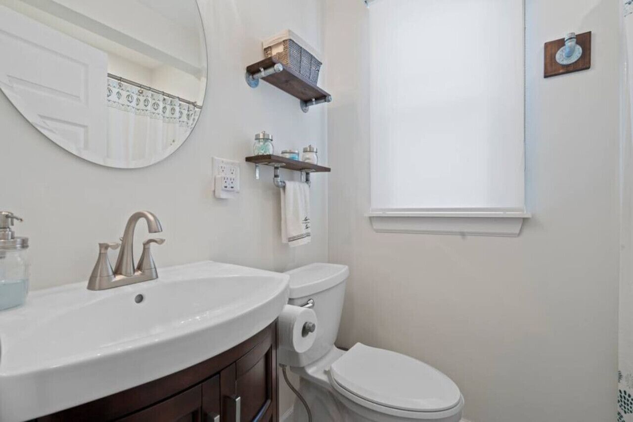 Une salle de bain avec un lavabo blanc, des toilettes et une fenêtre avec un rideau.