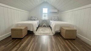 A room with two beds, a window, and a wooden floor.