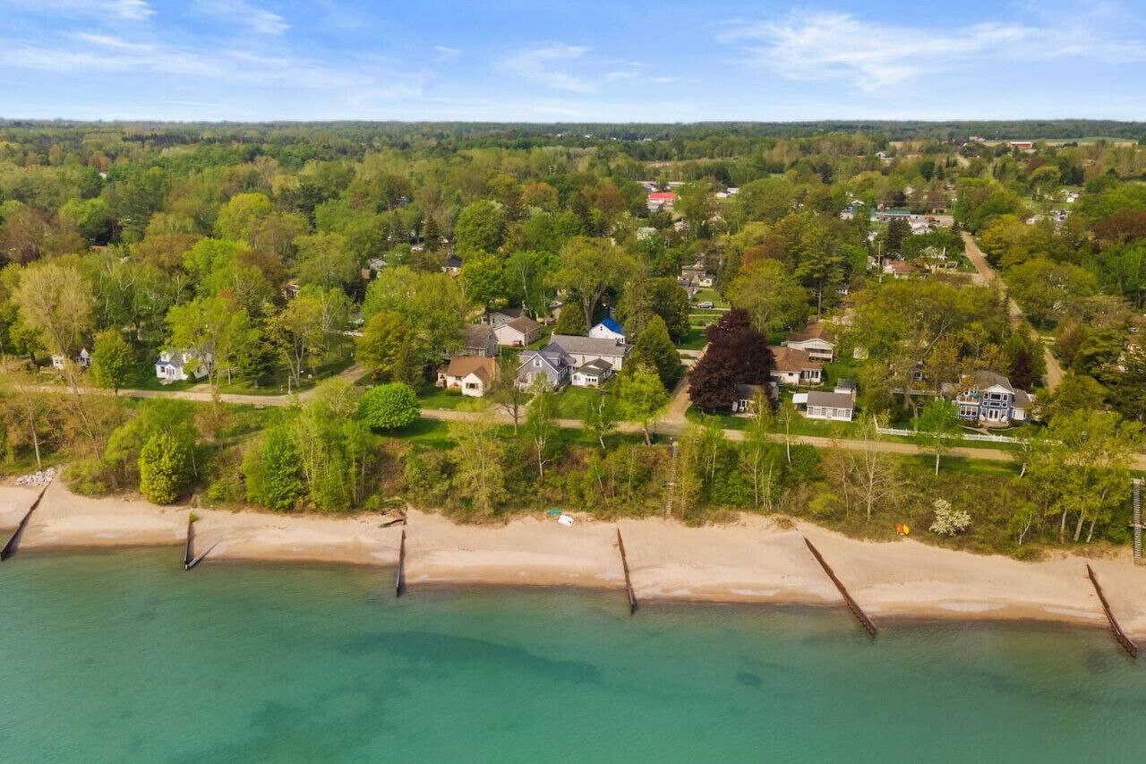 Vista aérea de una zona residencial costera con casas, una playa y cielo despejado.