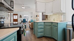 A kitchen with white cabinets, a teal island, and a dining area with a chair and table.