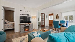 A cozy living room with a fireplace, a television, and a dining area with blue chairs.