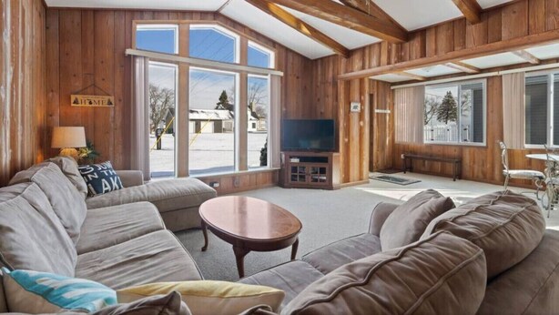 Ein gemütliches Wohnzimmer mit Holzwänden und -decken, einem großen Fenster, einem Flachbildfernseher und einem Sofa.