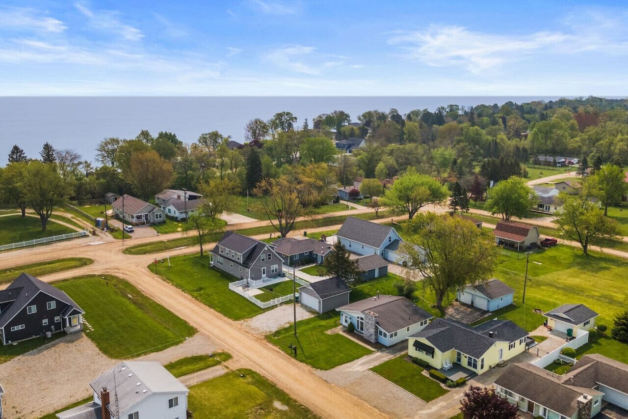 Vue aérienne d’un quartier résidentiel avec des maisons, des routes et une étendue d’eau en arrière-plan.