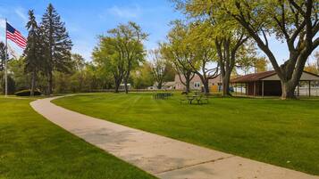 A park with a paved walkway, picnic tables, and a flagpole with an American flag.