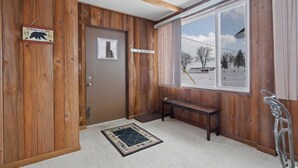 Ein Zimmer mit Holzwänden, einer Bank, einer Tür und einem Fenster mit Blick auf Bäume und ein Gebäude.