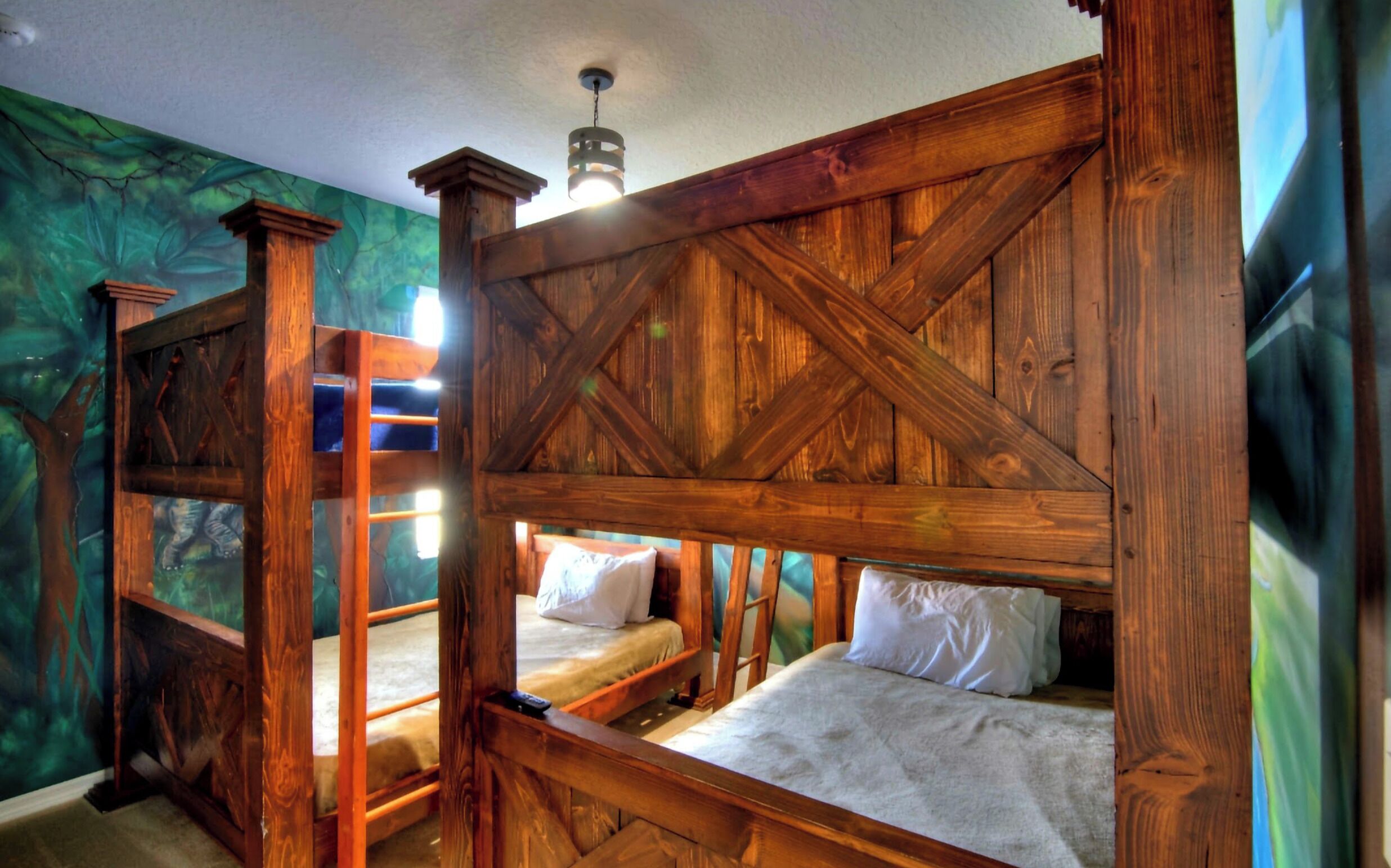 A rustic wooden bunk bed room with a ladder and a mural of a forest on the wall.