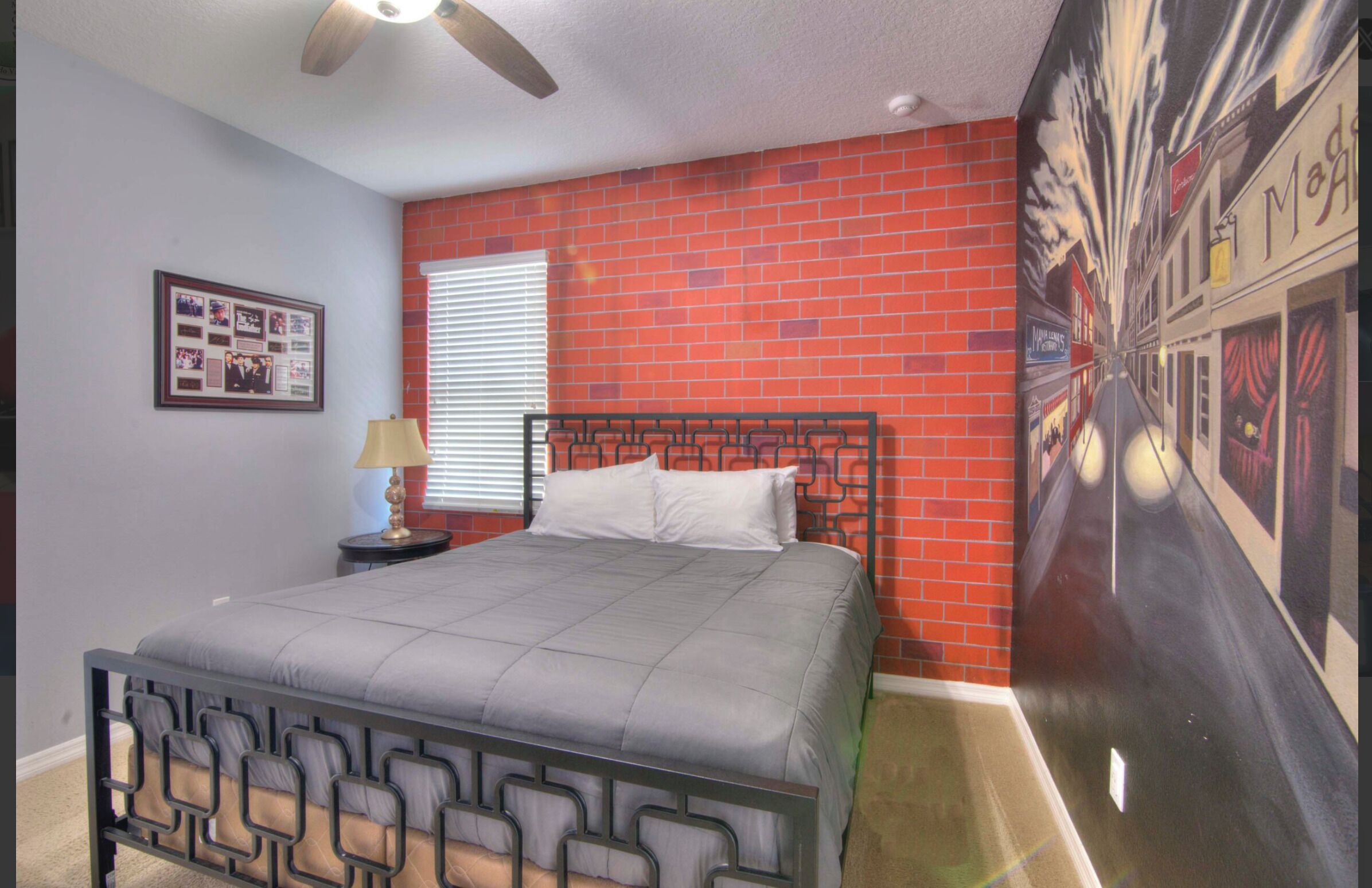 A bedroom with a bed, a nightstand, a lamp, a framed photo, and a brick wall.