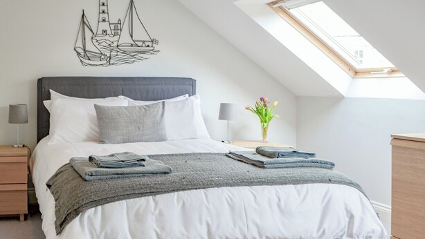 A bedroom with a bed, a skylight, a nightstand, a lamp, and a wall art piece. - 3 bedroom accommodation in Alnwick (Alnwick)