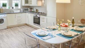 A modern kitchen with white cabinetry, a built-in oven, and a dining area set for six with clear glassware and plates. - 3 bedroom accommodation in Alnwick (Alnwick)