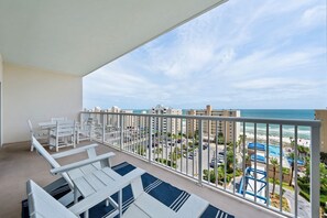 Un balcon avec des chaises blanches et une table, donnant sur une plage et une piscine.