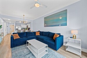 Een moderne woonkamer met een blauwe modulaire bank, een witte salontafel en een plafondventilator.