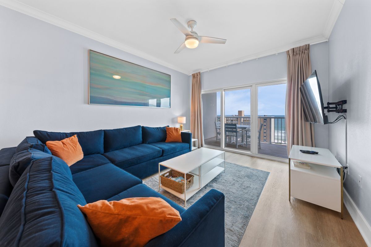 A modern living room with a sectional sofa, a coffee table, a TV, and a large window with a view of buildings.