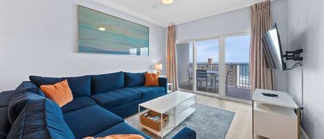 A modern living room with a sectional sofa, a coffee table, a TV, and a large window with a view of buildings.